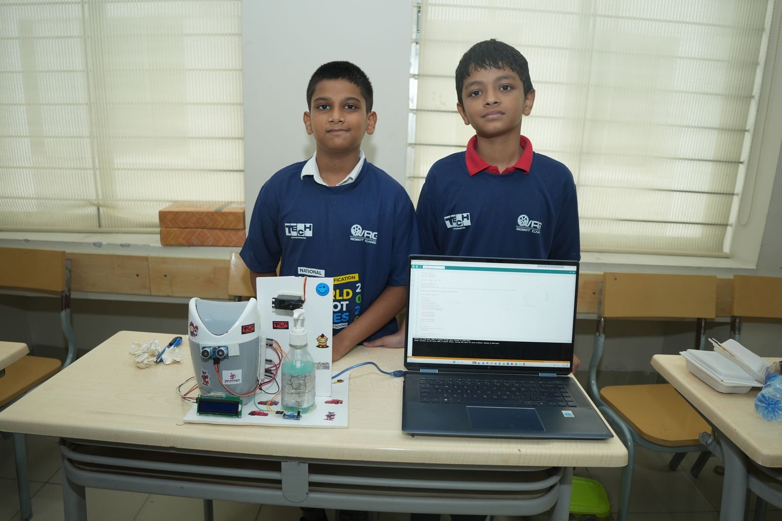 Two junior participants in WRG shirts stand behind their sensor-based project and laptop