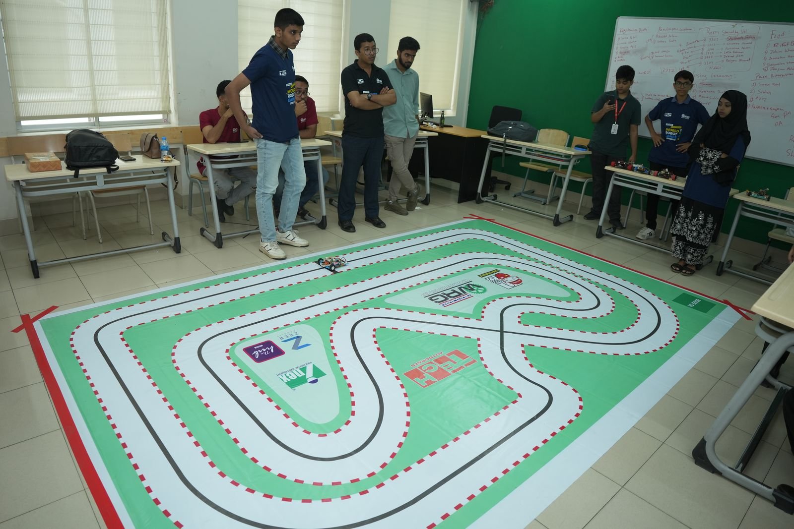 Students gather around a large green line-tracing track taped out on the classroom floor