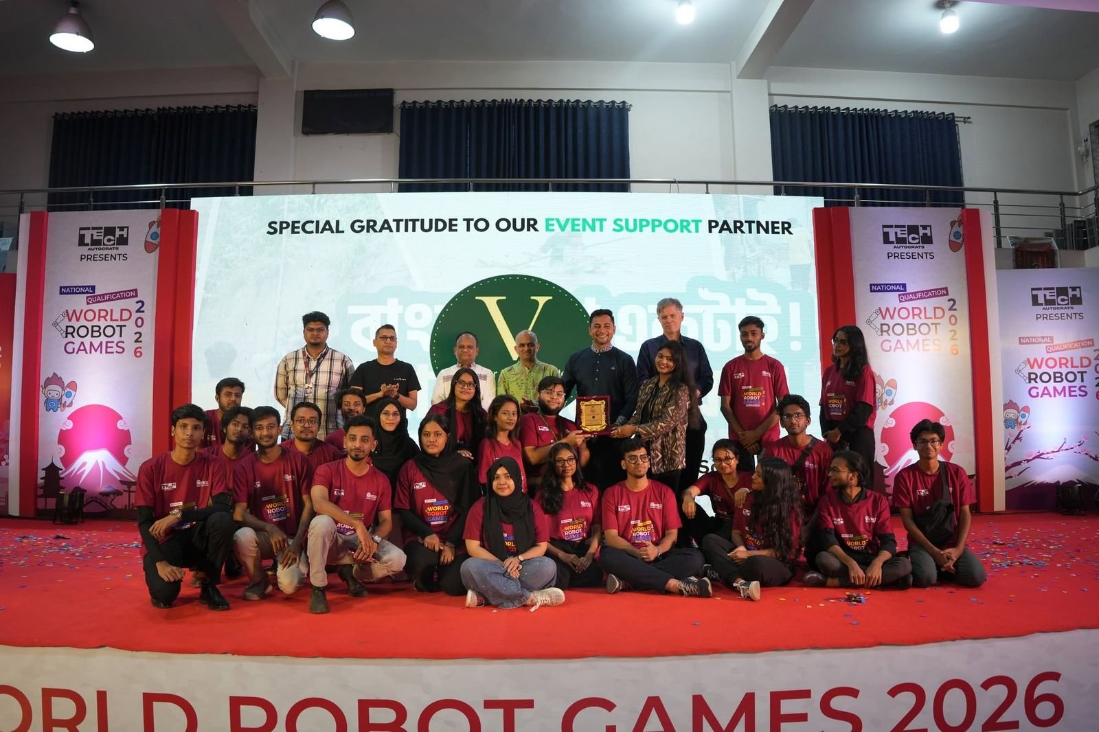 The event support team in maroon shirts gathered on stage beneath a World Robot Games 2026 banner