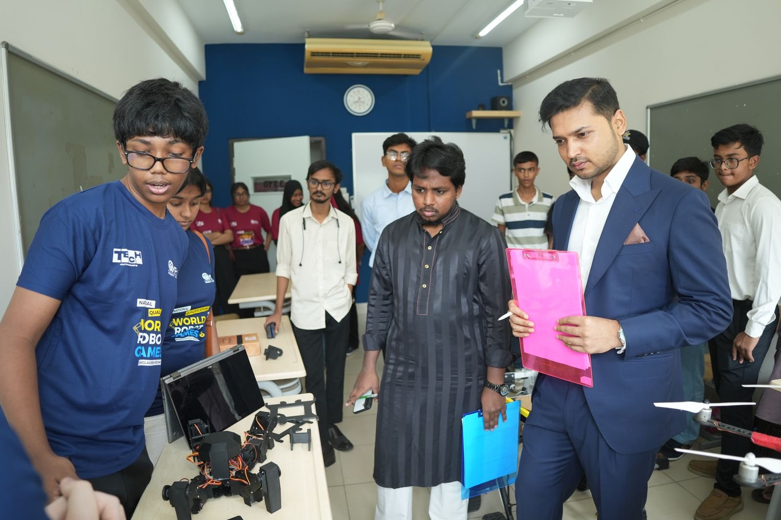 Judges with clipboards review a team's hexapod robot project