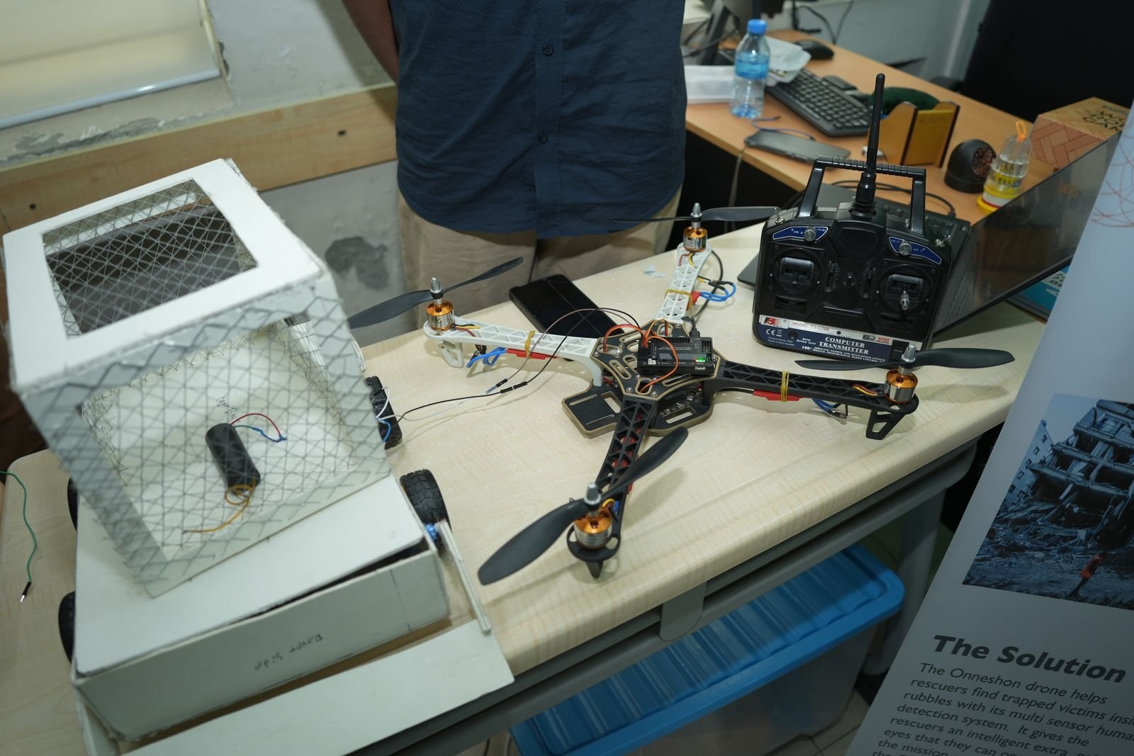 A quadcopter drone and its transmitter on display beside a caged enclosure