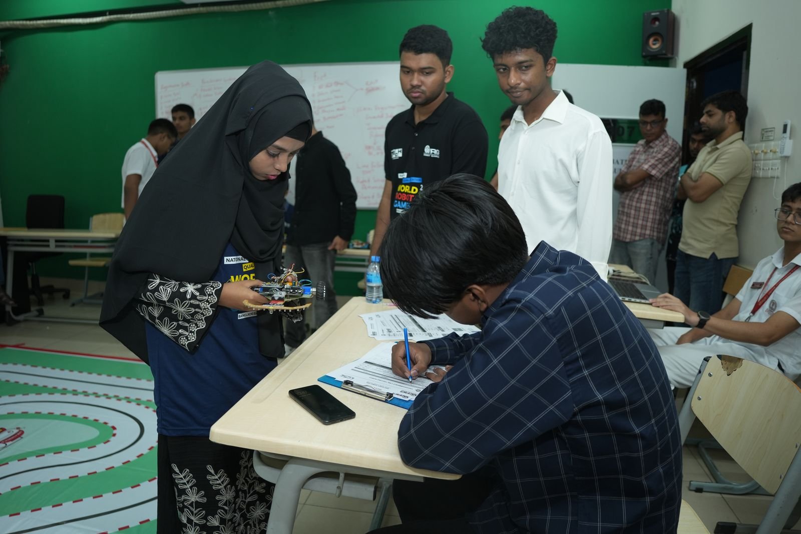 A participant holds her small robot while details are recorded at the judges' desk