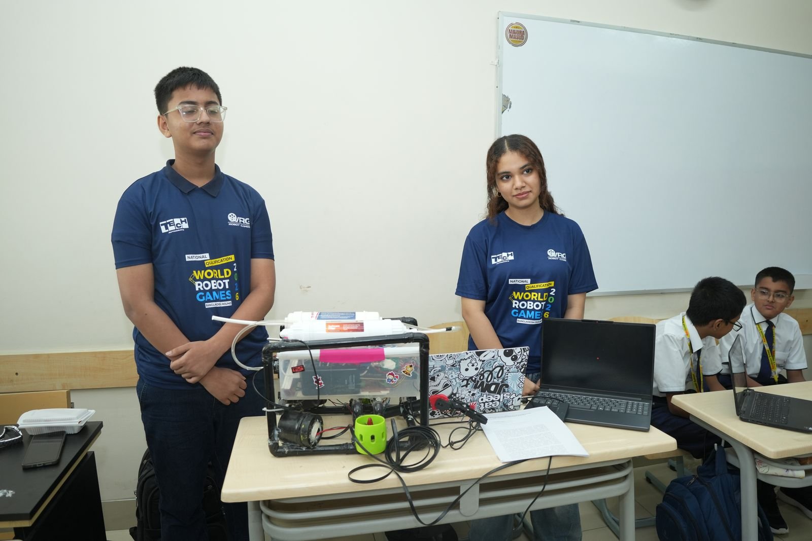 Two senior participants in WRG shirts present their project hardware at their desk
