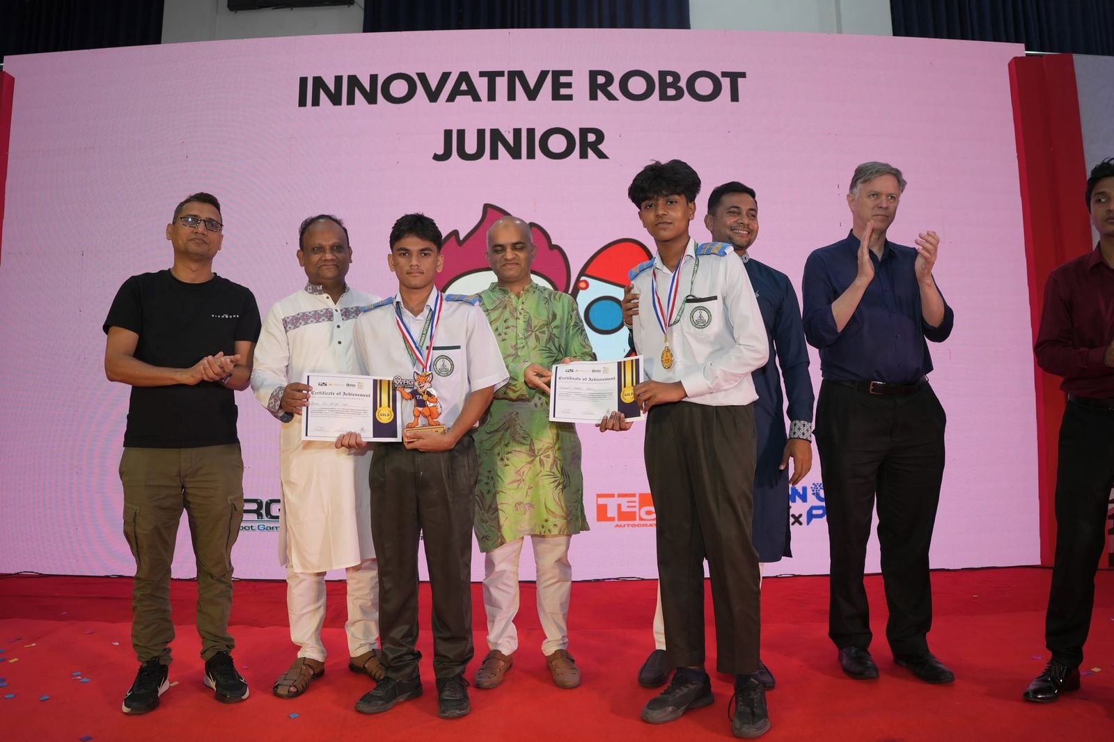 Two students in school uniform with gold medals and certificates, applauded by guests