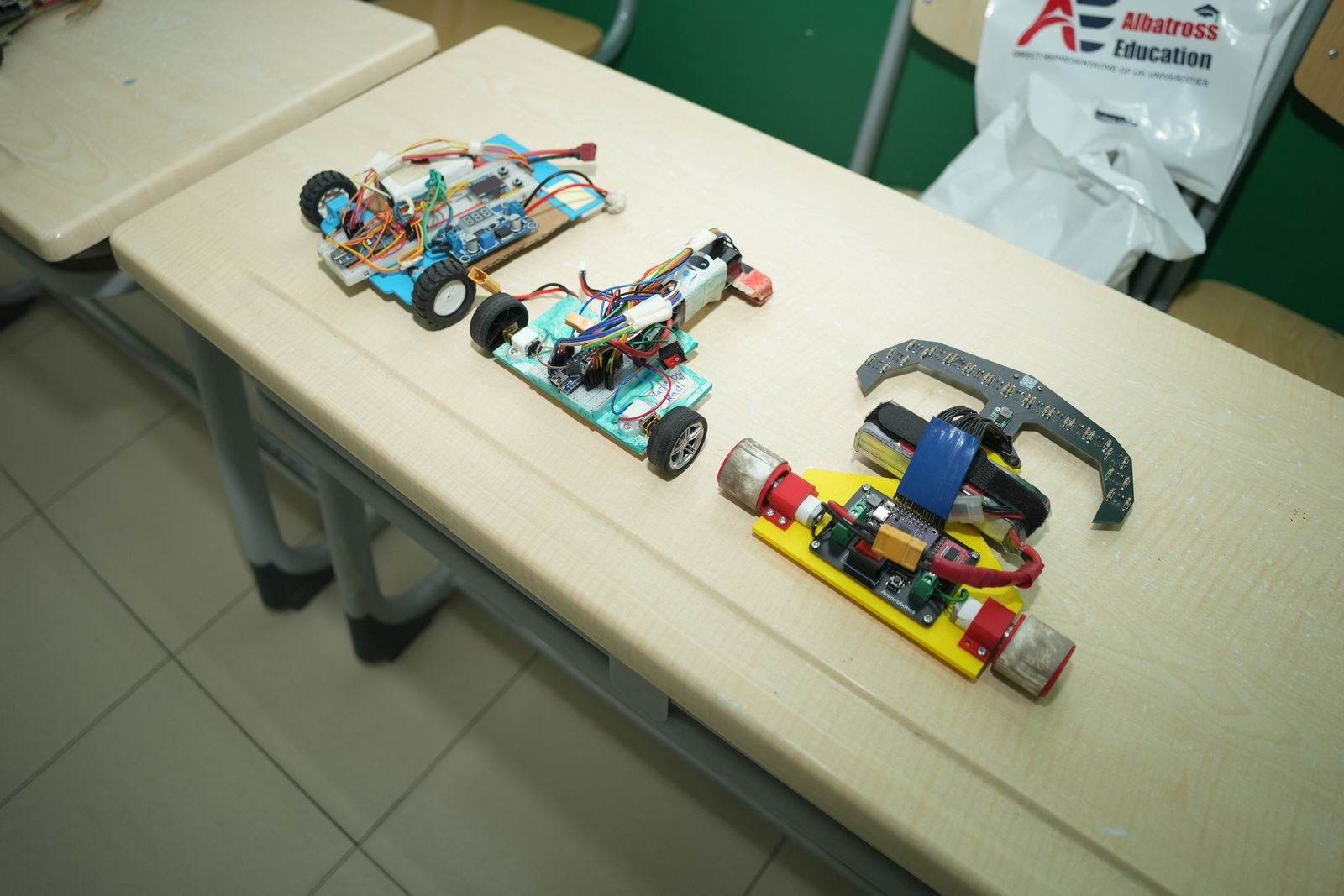 Two hand-wired line-follower robots and a yellow-chassis robot resting on a desk