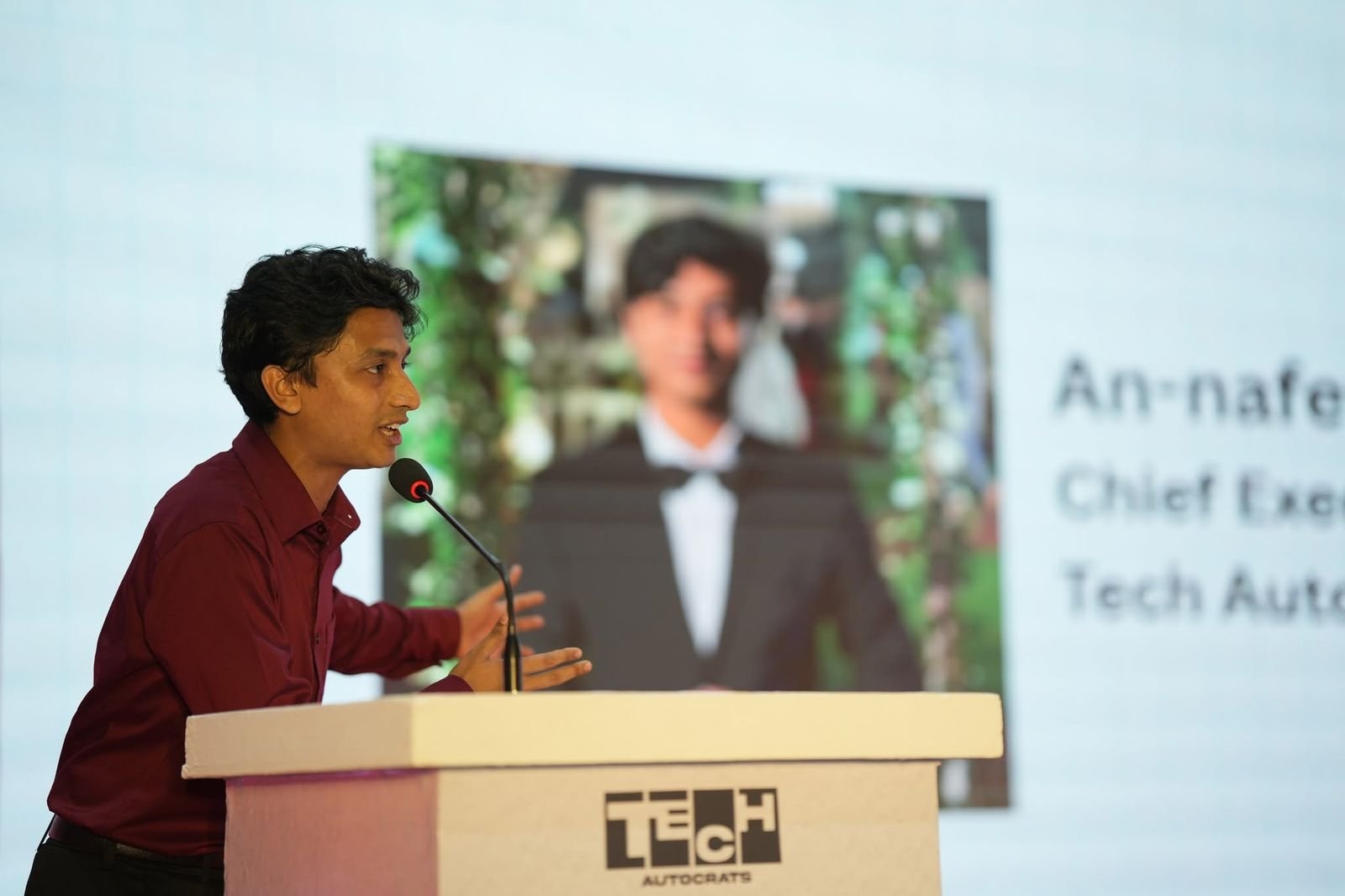 A speaker gestures while addressing the audience from the Tech Autocrats podium